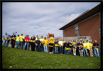 Most of the custodial services, grounds-keeping and maintenance team holds up their VIP gifts in front of a stone wall